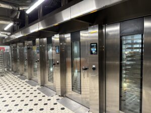 16 MIWE roll-in e+ Stikkenöfen bilden das Herzstück der neuen Rischart-Backstube. Sie ermöglichen das gleichzeitige Backen auf 18 Blechen pro Ofen und sorgen für konstante Ergebnisse – von der frischen Wiesn-Breze bis zum dreitägig geführten Dinkelbrot.. © Beigestellt