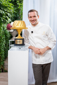 Philipp Zauner, Geschäftsführer der traditionsreichen Konditorei Zauner in Bad Ischl, ist Juror bei „Das große Backen Österreich“. Neben ihm steht der goldene Gugelhupf, um den acht Hobbybäcker in sechs Folgen auf Puls 4 und Joyn kämpfen.Bildcredit: © Puls 4 / Jörg Klickermann